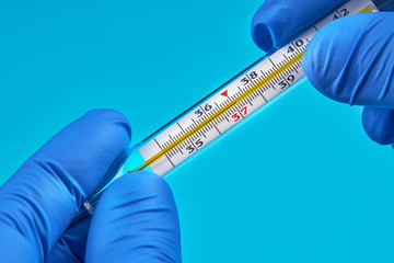  person in medical gloves holds mercury thermometer that show 37 temperature. virus and infection...