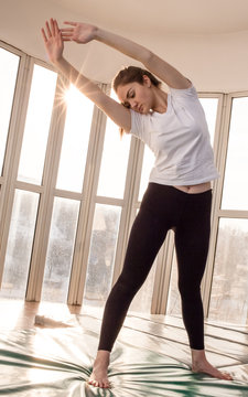 Woman Fitness Practice With Sun Shining Through The Window. Bending To The Side