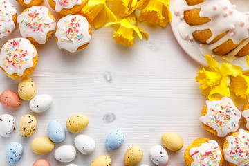 Easter background in cheerful colors with iced  cupcakes, chocolate eggs and daffodils on a white background with copy space 