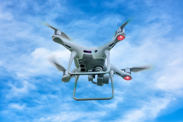 White drone quadcopter taking off from the ground on background of blue sky.