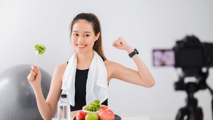 Beautiful asian woman healthy blogger is showing fruit and clean diet food. In front of the camera to recording vlog video live streaming at home.Fitness influencer on social media online.