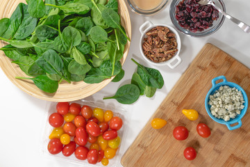 Salad ingredients close up, view from above.  Spinach, tomatoes, blue cheese, pecans, cranberries, and dressing on a kitchen table