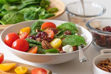 Baby spinach salad with tomatoes, cranberries, pecans, blue cheese and raspberry vinaigrette close up in a bowl on a kitchen table