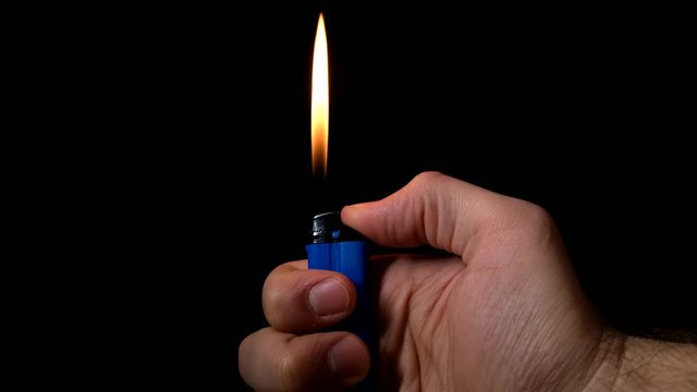 Close up view of male hand turning on blue gas lighter isolated on black.