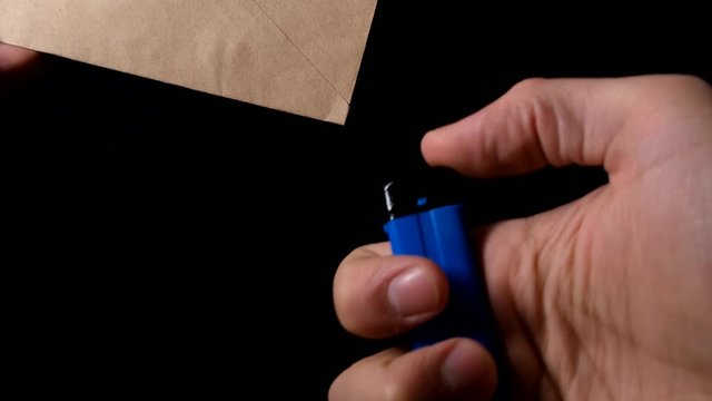 Close up view of male hand light up vintage paper envelope with zippo gas lighter isolated on black.