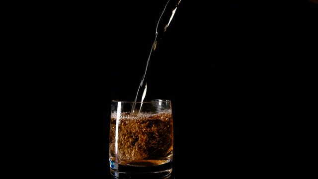 Whiskey pouring into glass isolated on black close up slow motion.
