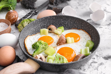 Frying pan with cooked eggs and vegetables on table