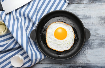 Frying pan with cooked egg on wooden background