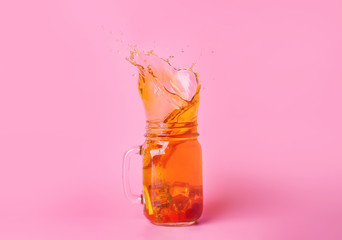 Mason jar of cold tea with splashes on color background