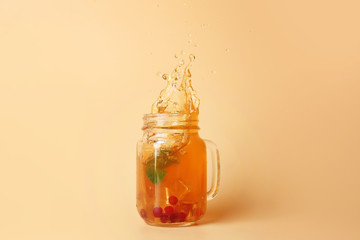 Mason jar of cold tea with splashes on color background