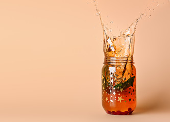 Mason jar of cold tea with splashes on color background