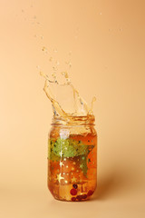 Mason jar of cold tea with splashes on color background