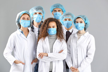 Group of doctors with protective masks on grey background. Concept of epidemic