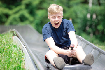 Happy teen boy riding at bobsled roller coaster rail track in summer amusement park