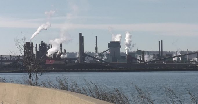 Large factory, with smoke stacks and lake in foreground