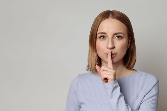 Shhh! European mysterious woman with short hair keep index finger over lips gesturing silence, isolated over grey background with copy space. Keep quiet, hush, privacy concept. 