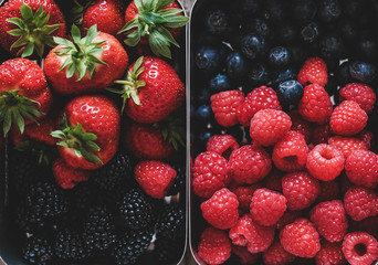 Healthy summer vegan lunch. Flat-lay of fresh seasonal strawberries, raspberries, blueberries and blackberries in metal lunchboxes, top view, close-up. Vegan, vegetarian, dieting, detox food