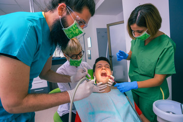 Team of dentists treating the teeth of their young boy patient using their dental tools.