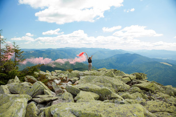 Beautiful woman with red colored smoke at the top of the mountain and cloudy sky background