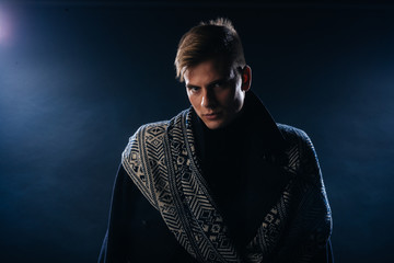 Portrait of a handsome with sharp jawline young man wearing a scarf while posing inside a studio on a black background..