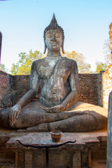 An old buddha statue in a historical park with tree and blue sky as background