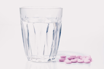 Pills and glass of water on white. High key shot.