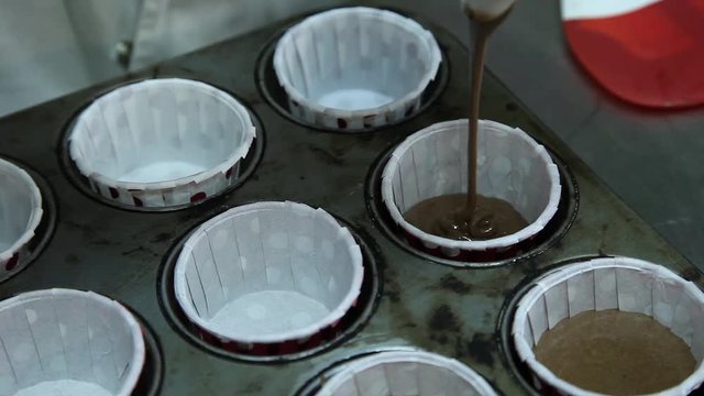 Confectioner putting liquid chocolate in baking cups for cupcakes pastery