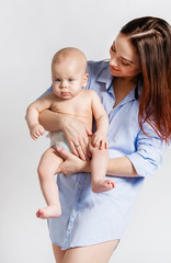 Mother in the shirt holding her baby over white background. The baby looks serious