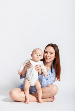 Mother In The Blue Shirt  With Child Baby Sitting On Floor In Studio Over White Background.