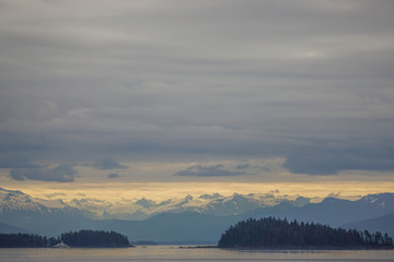 Alaska, USA: Snow-capped mountains under a cloudy sky, a cruise ship sailing through islands in the Inside Passage.