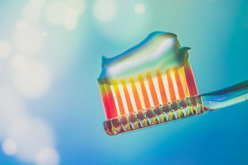Orange plastic toothbrush with a toothpaste on a blue background. Side view. Art bokeh with copy space.