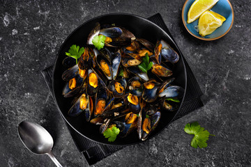 Close up of a black plate with mussels on black background