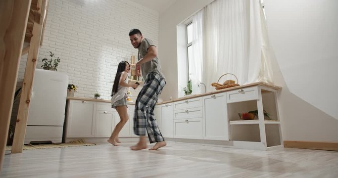 Pretty interracial couple wearing pyjamas funnily dancing and singing early in morning, preparing for new day, spending time together, having fun 4k