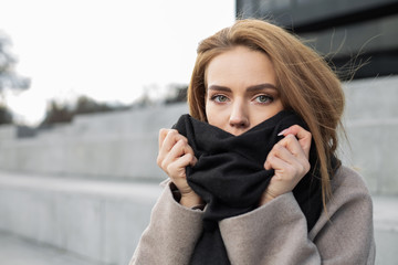 Fototapeta premium Pretty girl wraps herself in a scarf on the street