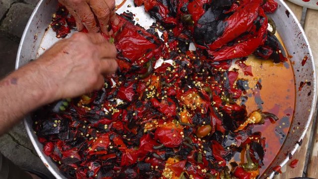 Cleaning grilled red peppers with a knife and bare hands. View from above