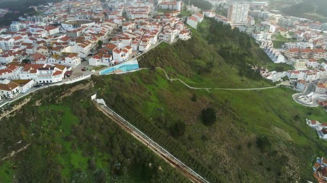 Aerial view (tilt down, 4k)  of skyline and Ascensor da Nazare or Nazare Funicular in a foggy day .Nazare is considered  the most popular seaside resorts in Silver Coast