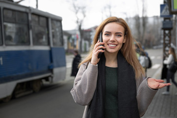 Girl talking on a smartphone at a tram stop.