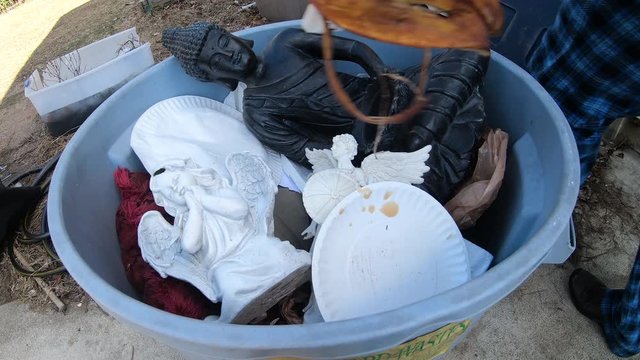Religious statues in garbage can with trash being tossed on top 4k slow motion.