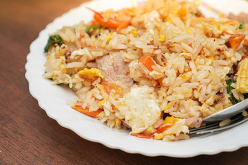 Close up and focus on fried rice mixed with various vegetables and meats in white plate place on dark brown wooden table