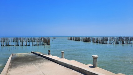 Naklejka premium Concrete pier beside seashore with bamboo pole for protection wave and blue sky background.