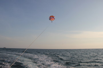 A young man and a girl are flying on a double parachute behind a boat over the sea.