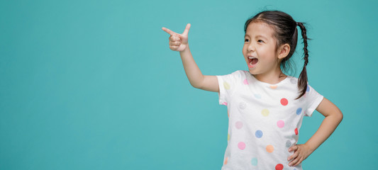 Beautiful smiling Asian little girl pointing hand to blank speech bubble, empty space in studio shot isolated on colorful blue background, Educational concept for school