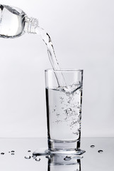 Pouring fresh pure water from bottle into a glass on the table with water drops, Healthcare and beauty hydration concept