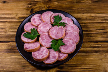 Black plate with sliced sausage on a wooden table