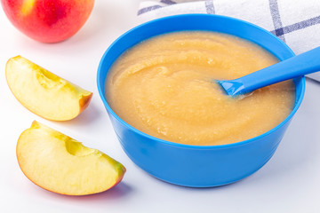 Baby food. Fresh homemade applesauce. Blue bowl with fruit puree on fabric and cut apples on table. The concept of proper nutrition and healthy eating. Organic and vegetarian food. Copy space for text