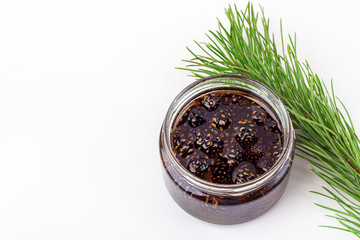 Unusual jam from pine cones in glass jar on white background among pine branches and cones. Organic...