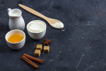 Baking background. Ingredients for cooking cake (flour, egg, milk, anise, cinnamon, cane sugar) in bowls on dark table. Food concept. Close up layout, copy space for text