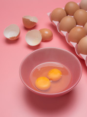 Eggs in bowl with eggshell on pink background
