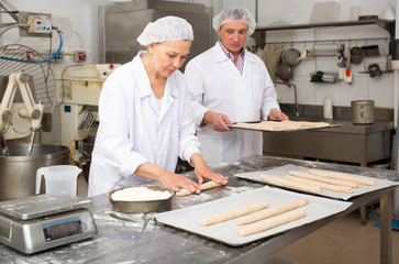 Woman forming baguettes from dough in bakery