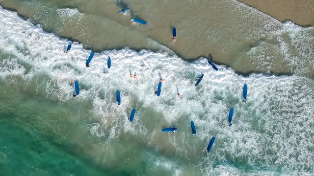 Aerial drone video of a group of surfers on blue boards having fun in the surf